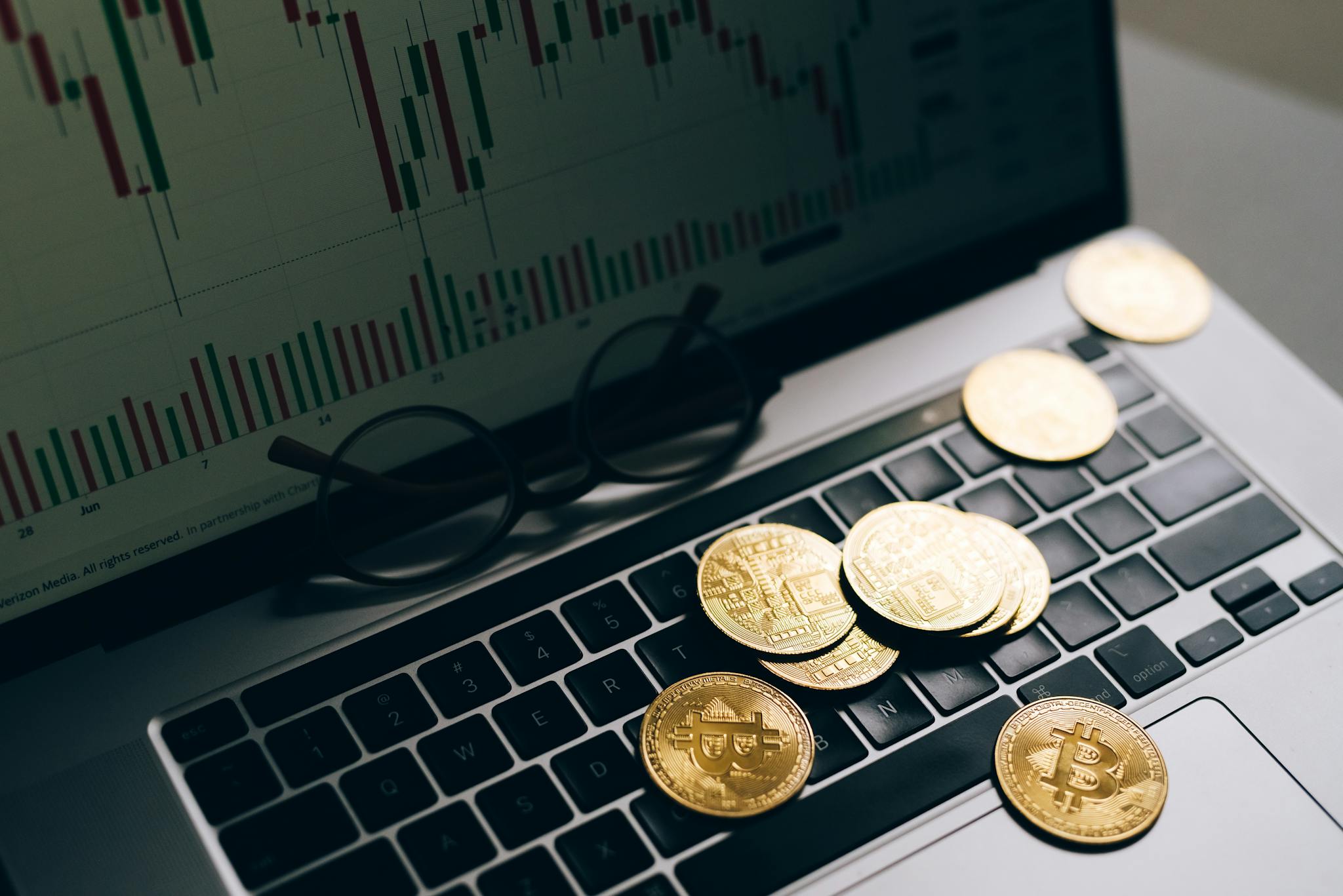 Golden Bitcoins on a laptop keyboard with a stock market chart on the screen, symbolizing cryptocurrency trading.
